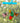 hand-painted butterfly mobile featuring 4 colorful butterflies and a red flower hanging from a blue crosspiece with a blurred green background

