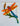 A colorful  pvc dragonfly bracket for mounting on a mailbox or porch post.  The dragonfly features bright orange wings, a red and blue head, a striped blue tail, green leaves, and a brown cattail above it.