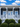 Navy house with white porch and palm tree decorative brackets on columns under a blue sky with clouds.