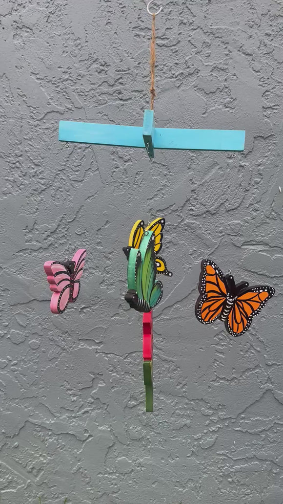 hand-painted butterfly mobile featuring 4 colorful butterflies and a red flower hanging from a blue crosspiece moving gently in the breeze

