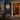A backlit white snowflake wall decor made from white weather-resistant pvc mounted on the dark blue siding of a house, shown next to a wooden front door with a wreath and small potted trees at dusk.